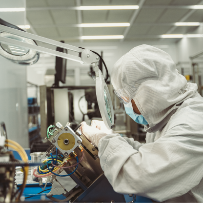 Cleanroom technician assembling wired equipment under a magnifier lamp