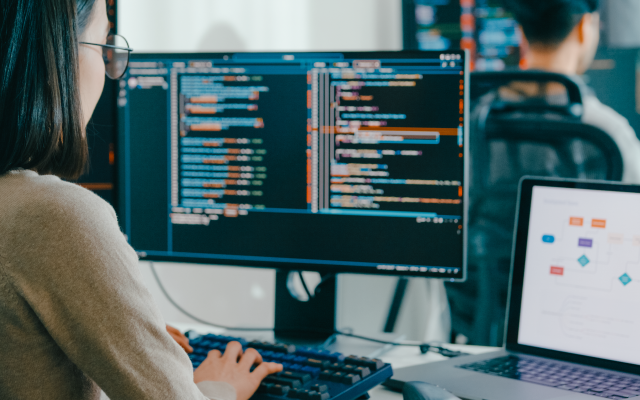 Software engineer working at dual monitors of code with a laptop showing a flowchart