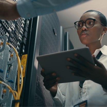 Engineer holding a tablet while inspecting a server rack with yellow network cables