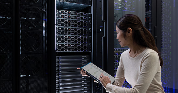 A technician at a server rack holding a component, data center aisle behind
