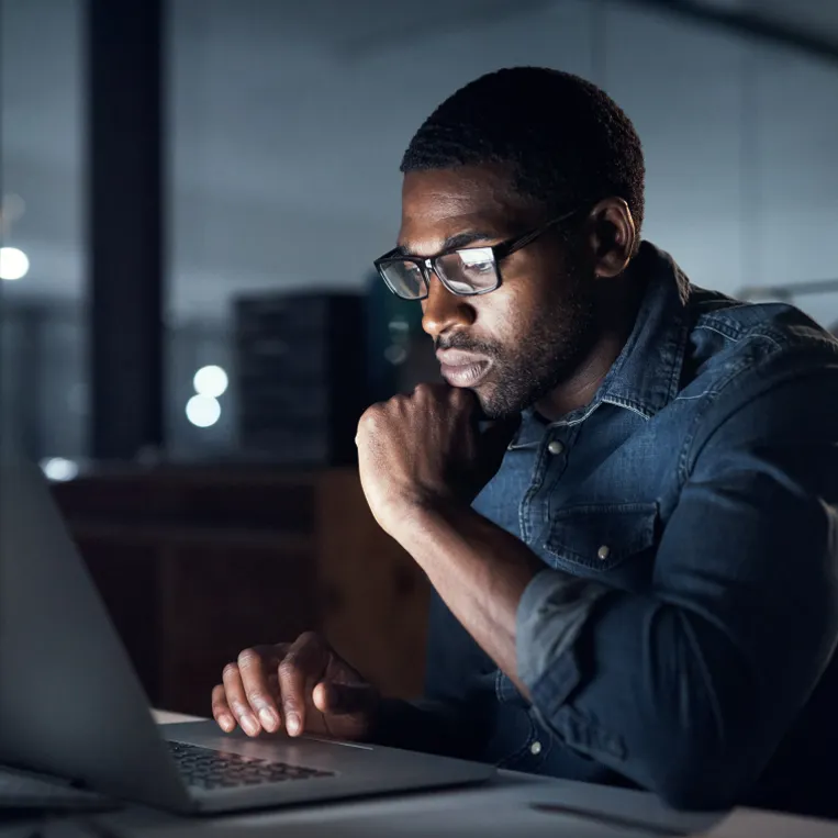 Man works on laptop in dimly lit office during evening