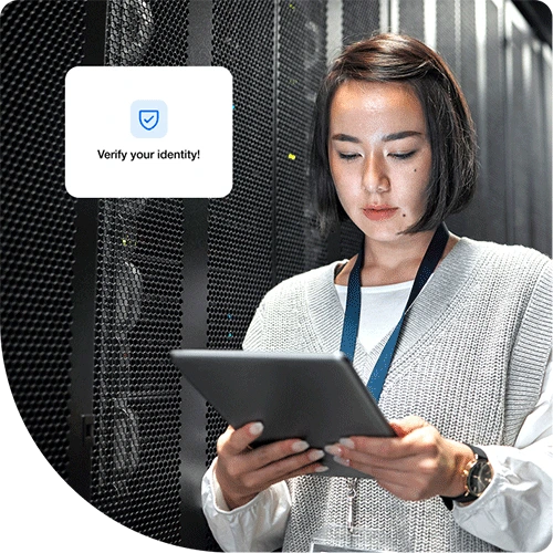 A woman with short dark hair is standing in a server room, holding and working on a Duo trusted device.