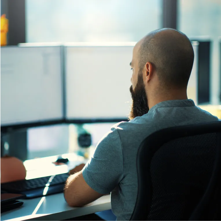 Person at desk with multiple monitors in sunlit room