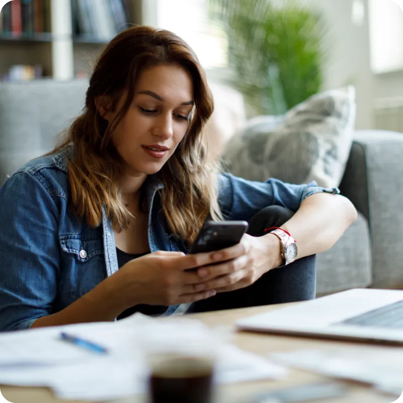 Person in denim shirt on couch holding smartphone