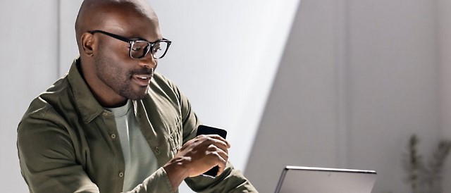 A man wearing glasses and a green jacket looking at a laptop.