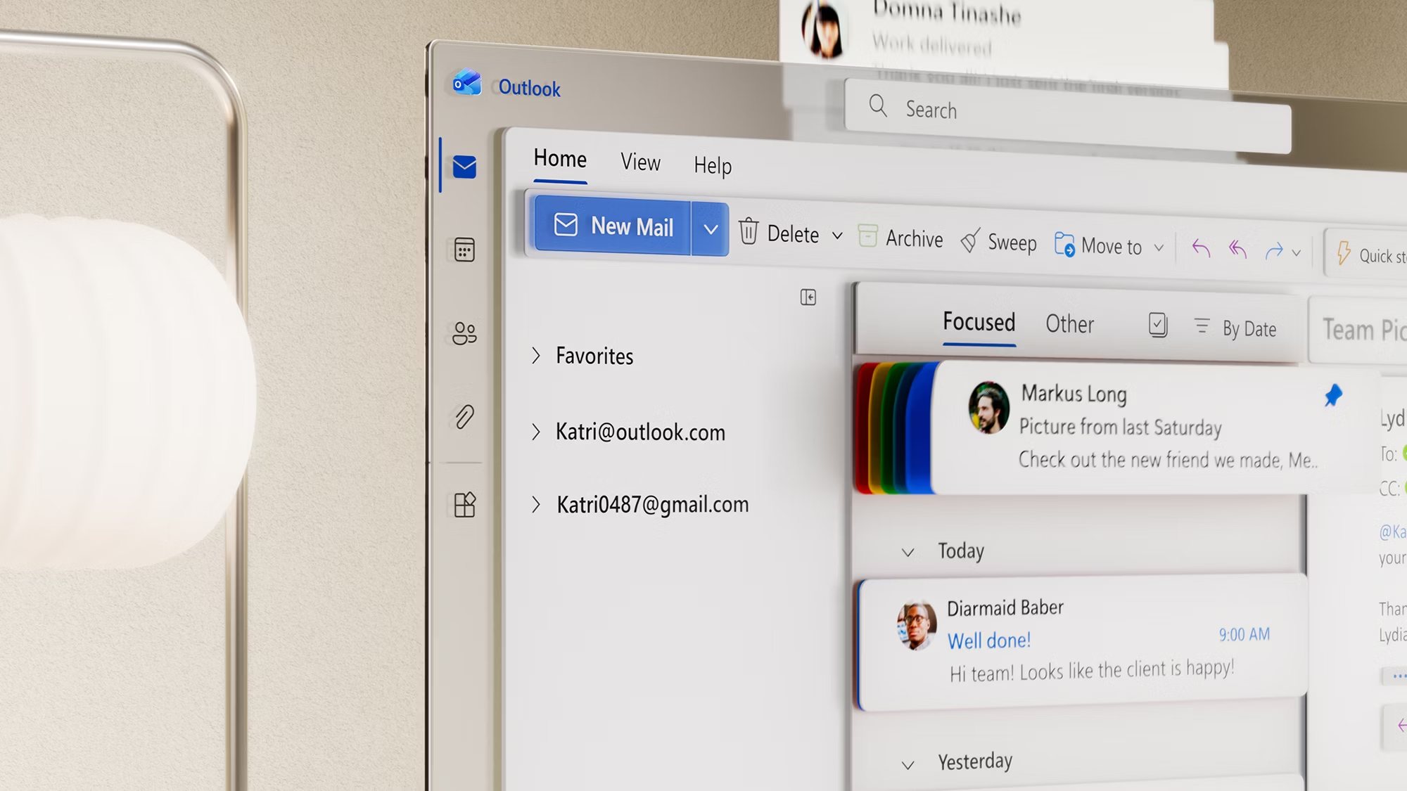 An Outlook inbox open on a screen beside a rounded desk lamp.