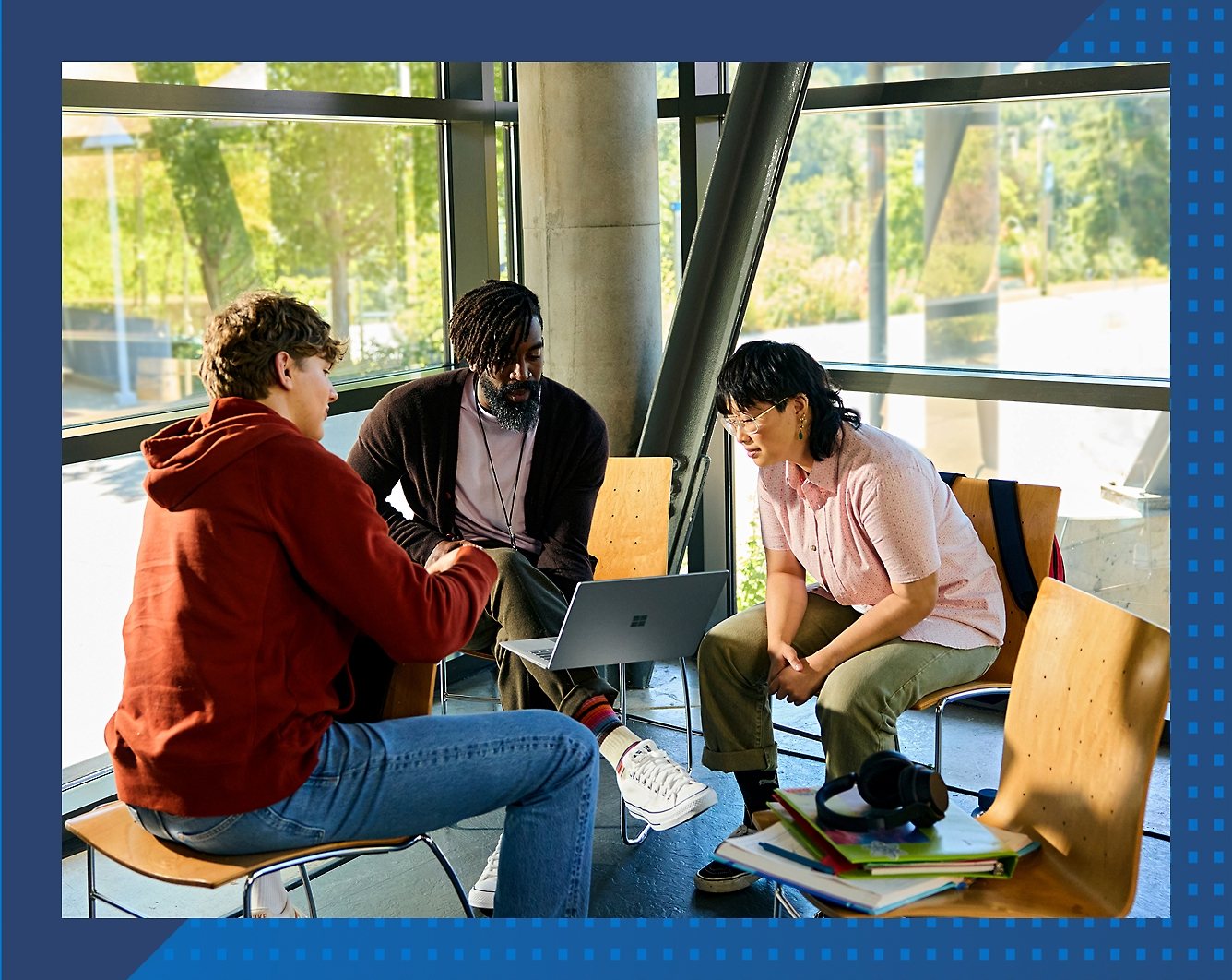 Three people seated in a modern space reviewing content together on a laptop.
